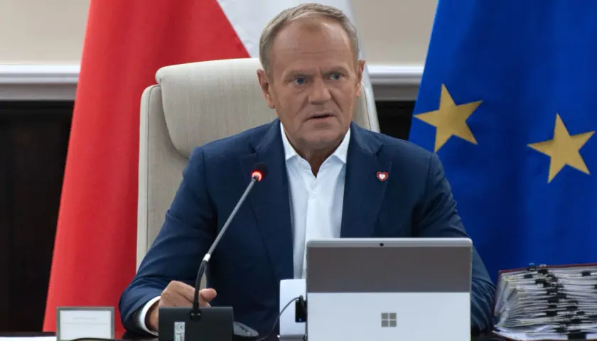 Donald Tusk siedzi przy stole, za nim flagi Polski i UE. Fani Konfederacji zarzucają rządowi "przeklejanie agendy eurokratycznej".