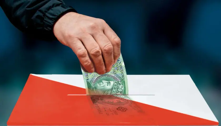 Dłoń wrzuca banknot 100 zł do urny w barwach narodowych.