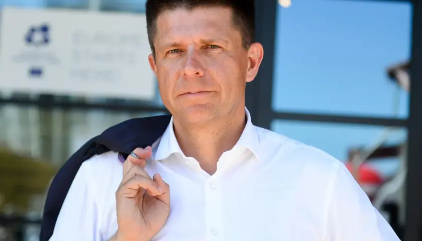 Ryszard Petru w białej koszuli, z marynarką na ramieniu, na tle budynku.