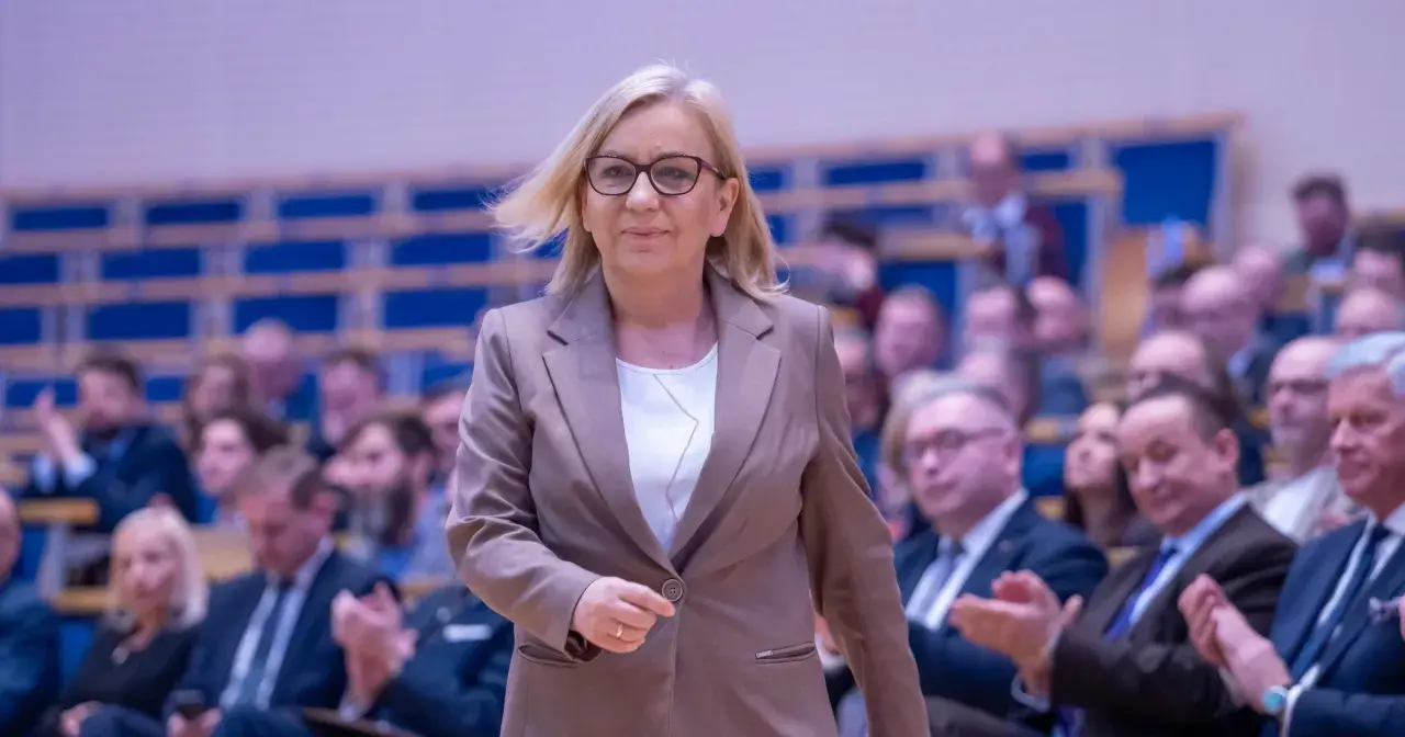 Kobieta w garniturze, minister klimatu, idzie przez salę pełną ludzi. Konfederacja ujawnia prawdziwe powody dla których złożyła wniosek o odwołanie ministry klimatu.