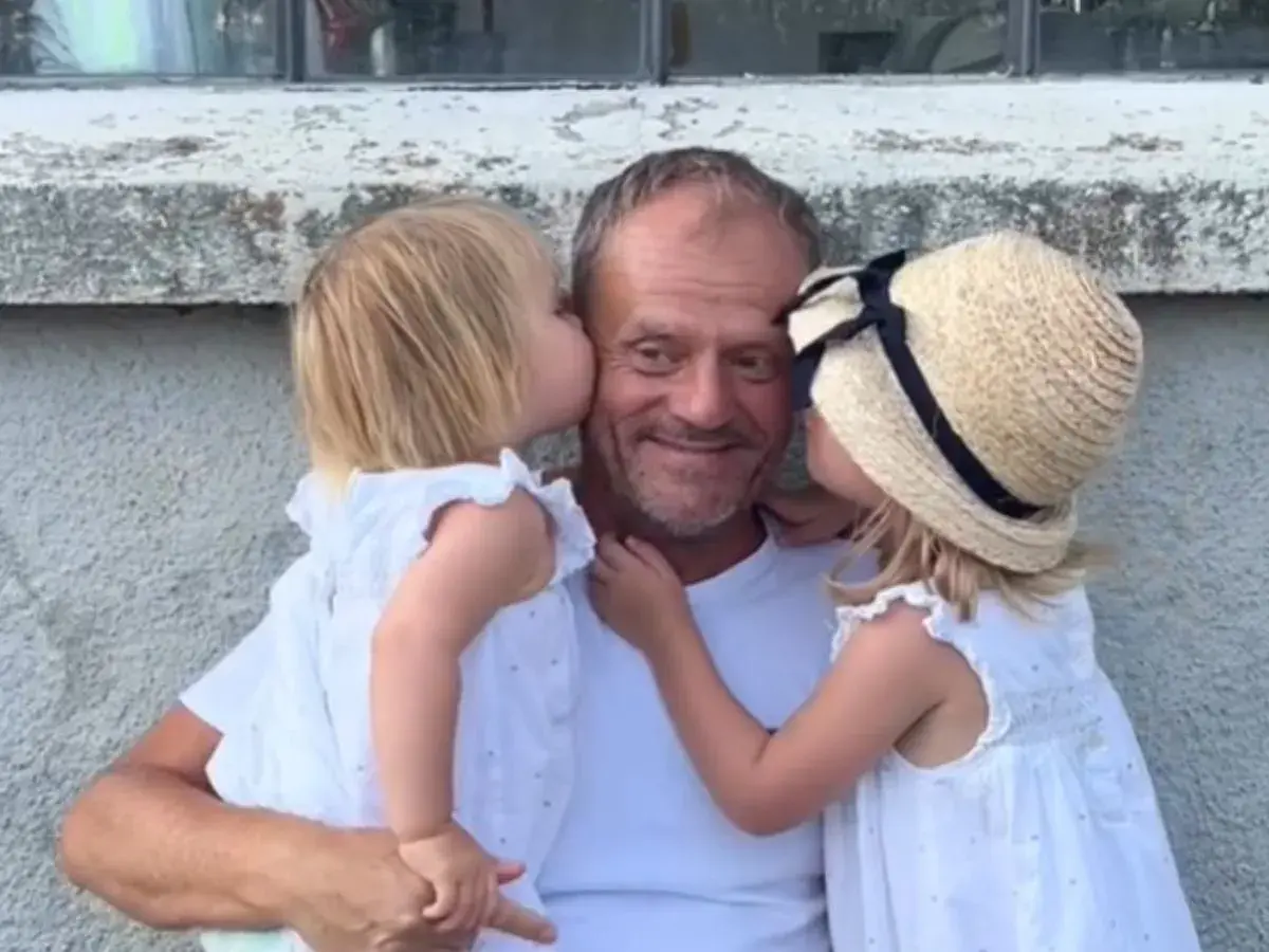Donald Tusk z dwiema córkami całującymi go w policzki.