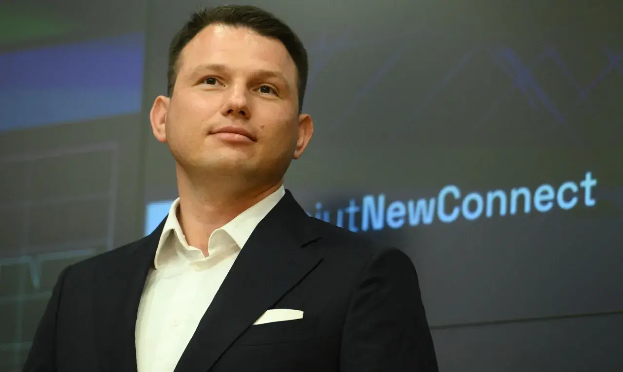 Kto finansuje luksusowe spotkania wyborcze Mentzena w największych miastach Polski? Mężczyzna w garniturze na tle ekranu z napisem "NewConnect".