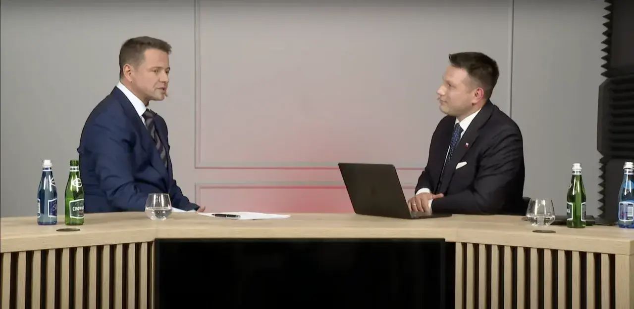 Sławomir Mentzen w garniturze siedzi przy biurku z laptopem, rozmawiając z drugim mężczyzną. Czy to dowód, dlaczego Sławomir Mentzen unika debat z kandydatami Koalicji Obywatelskiej?