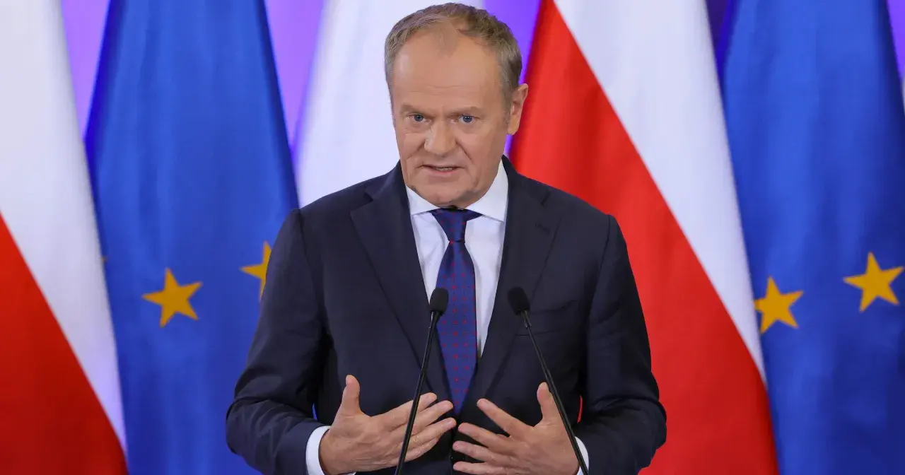 Donald Tusk w garniturze przemawia przed flagami Polski i Unii Europejskiej.