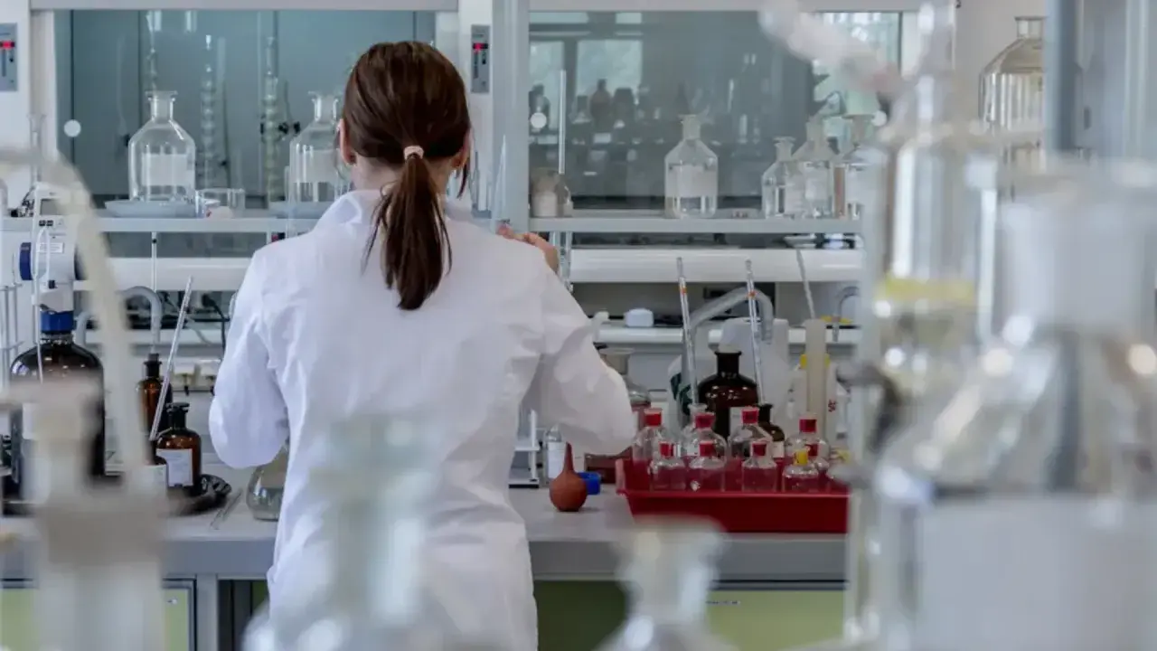 Naukowczyni w białym fartuchu pracuje w laboratorium z probówkami i odczynnikami.