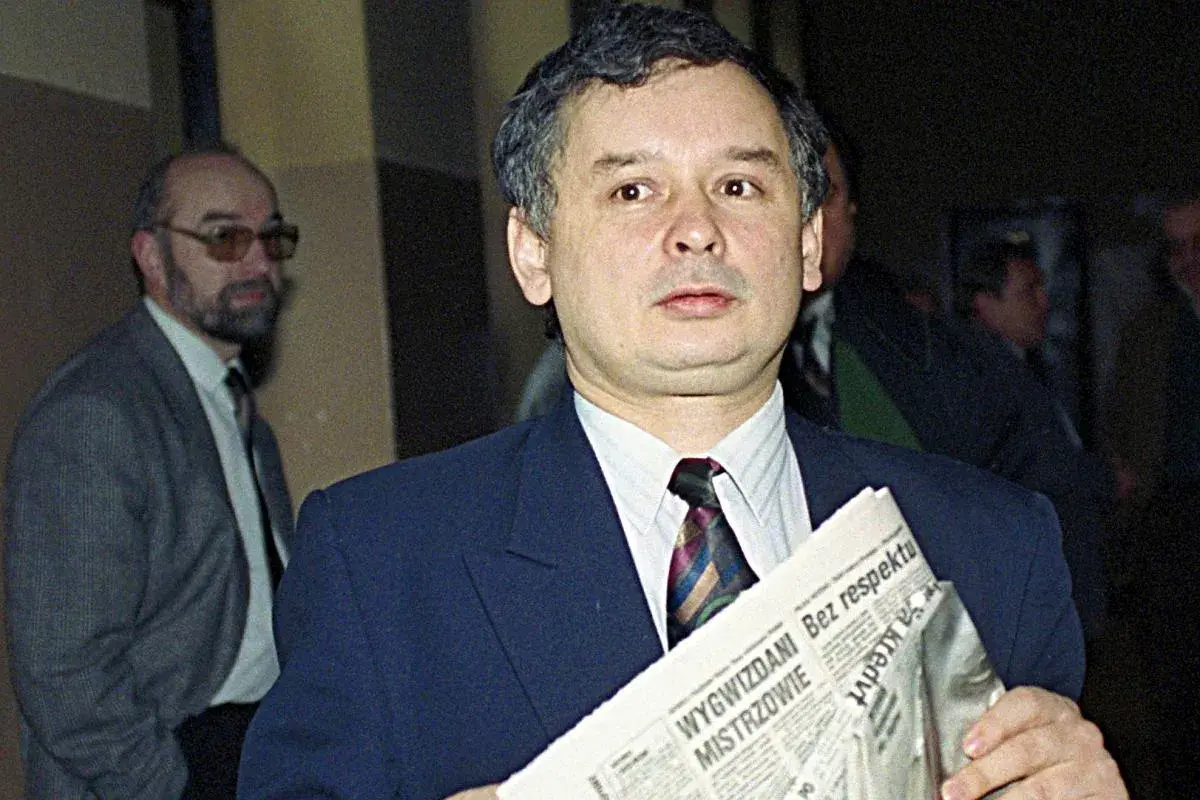 Jarosław Kaczyński z gazetą, zastanawia się, kto ze starej gwardii PiS trafił na "czarną listę". Obok mężczyzna w okularach.