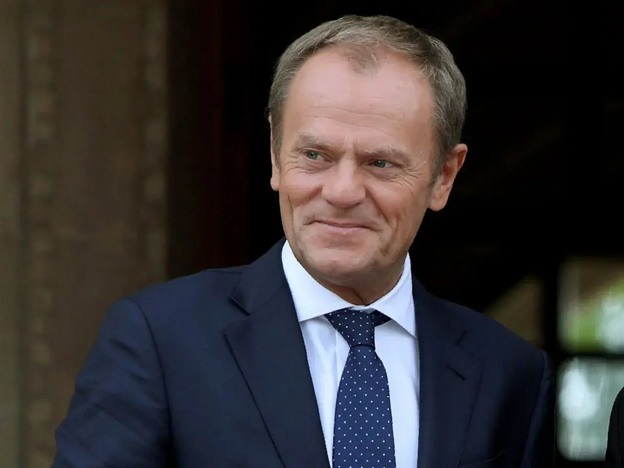 Donald Tusk w garniturze i krawacie, uśmiecha się.