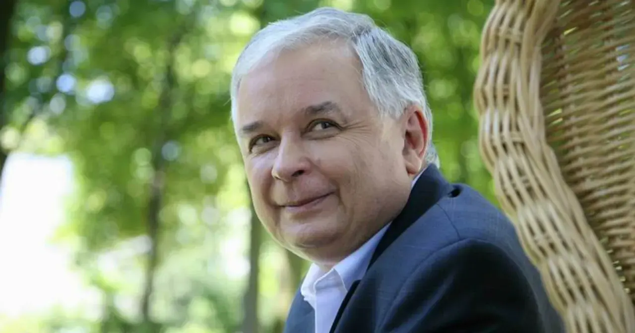 Lech Kaczyński w garniturze siedzi na tle zieleni i wiklinowego fotela.