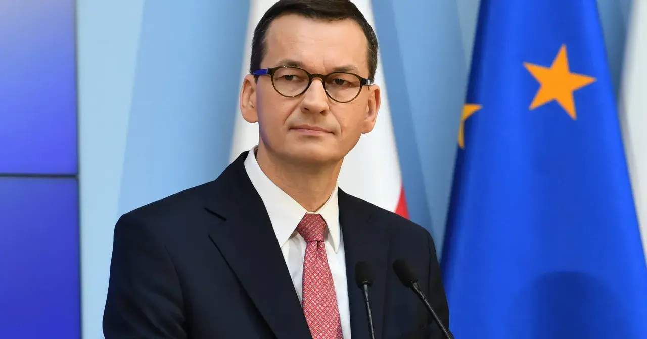 Mateusz Morawiecki w garniturze i okularach, na tle flag Polski i UE.