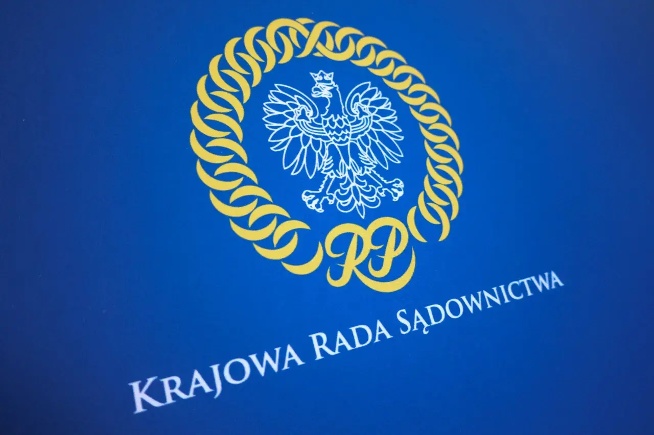 Herb RP i napis "KRAJOWA RADA SĄDOWNICTWA" na niebieskim tle. Symbolika nawiązuje do prawdziwych przyczyn konfliktu wewnątrz KO o zasady powoływania nowej KRS.