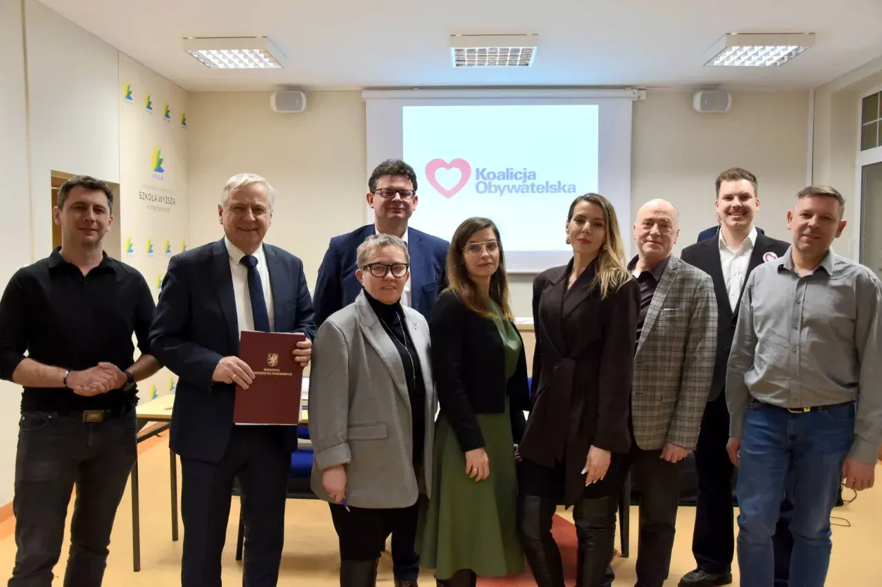 Grupa osób pozuje do zdjęcia przed ekranem z logo Koalicji Obywatelskiej.