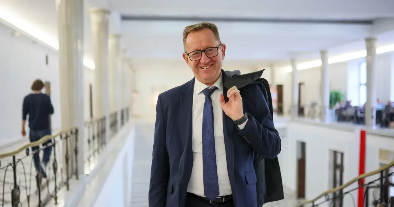 Uśmiechnięty mężczyzna w garniturze, który może być powiązany z pytaniem, dlaczego Robert Telus i Rafał Romanowski zostali zawieszeni w prawach członka.
