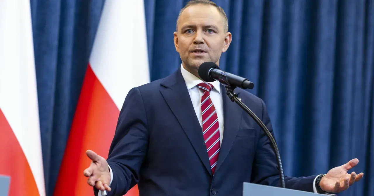 Mężczyzna w garniturze przemawia przy mikrofonie na tle flagi Polski. Czy prezydent faktycznie planuje ogłosić stan wyjątkowy w związku z sytuacją na wschodzie?
