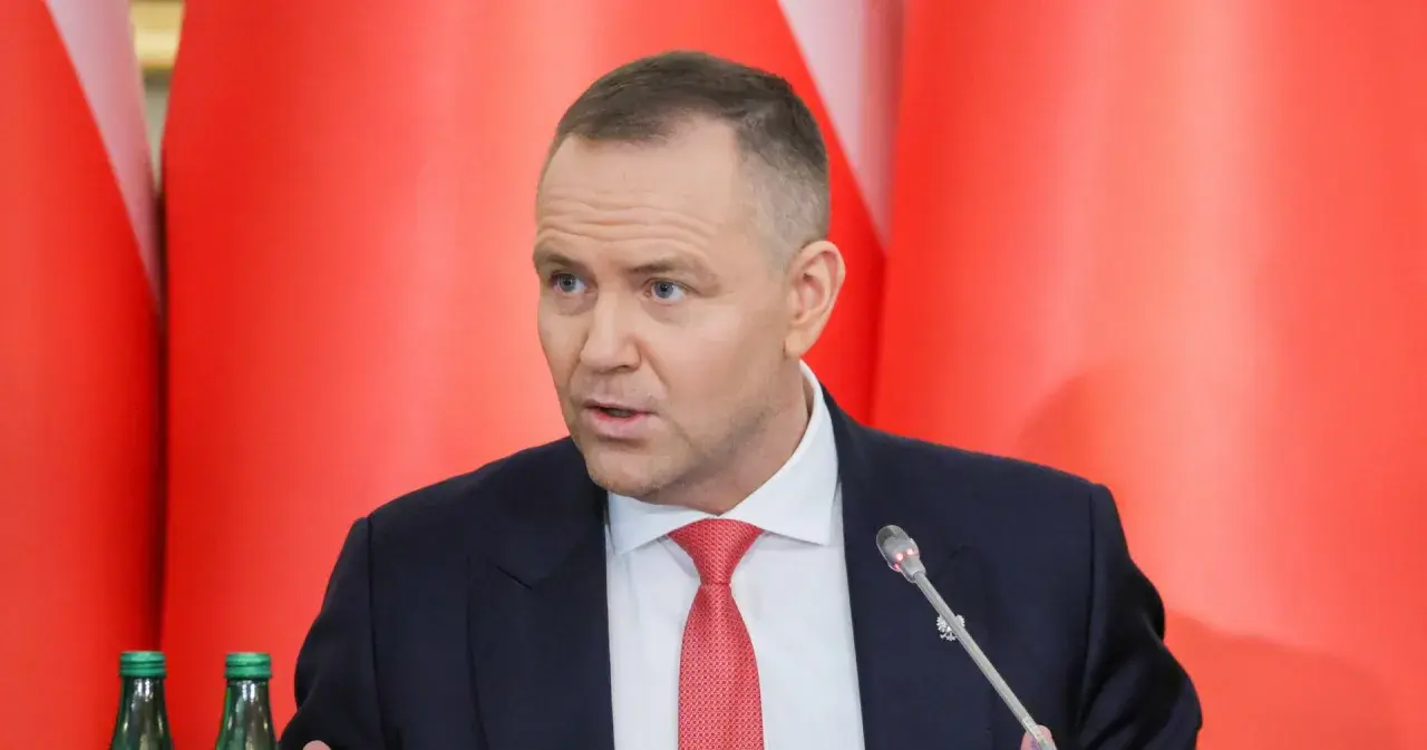 Mężczyzna w garniturze i czerwonym krawacie przemawia na tle czerwonych flag. Dyskutuje, dlaczego prezydent zapowiada veto wobec ustawy o wyborze sędziów do KRS.