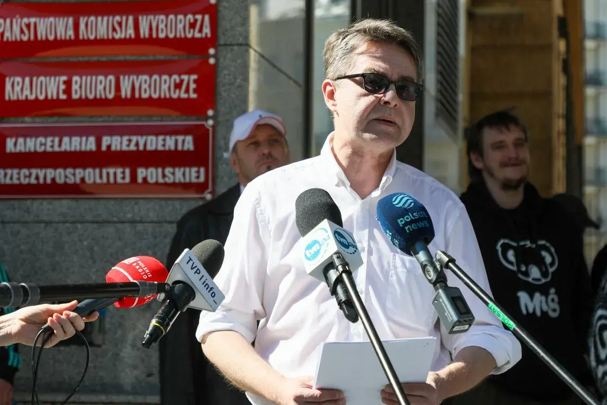Mężczyzna przemawia do mediów przed budynkiem z napisem "Kancelaria Prezydenta RP". Dyskutuje się, dlaczego Pałac Prezydencki został wyłączony z części audytów dotyczących lotów państwowych.