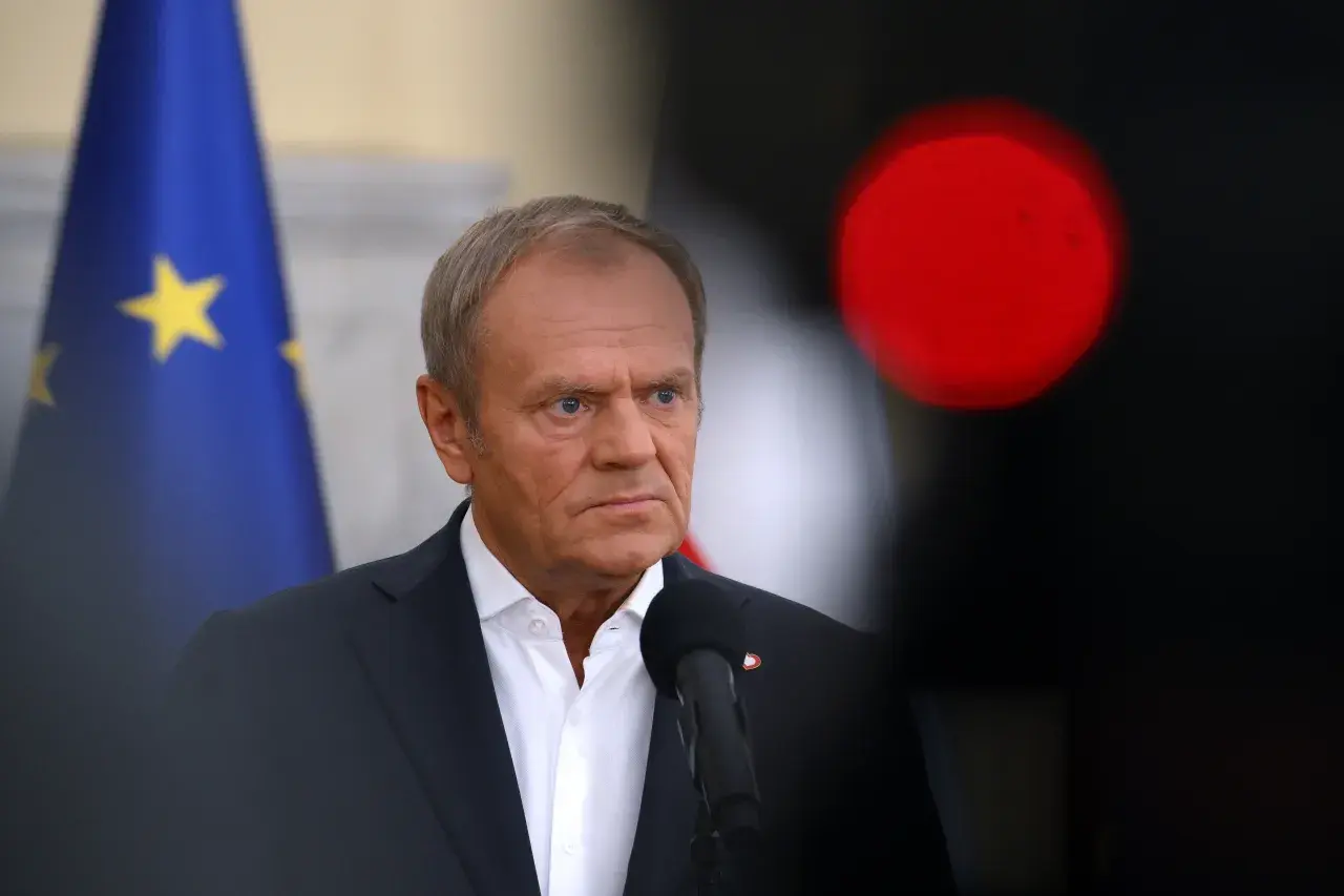 Donald Tusk w garniturze, z flagą UE w tle i czerwonym światłem.
