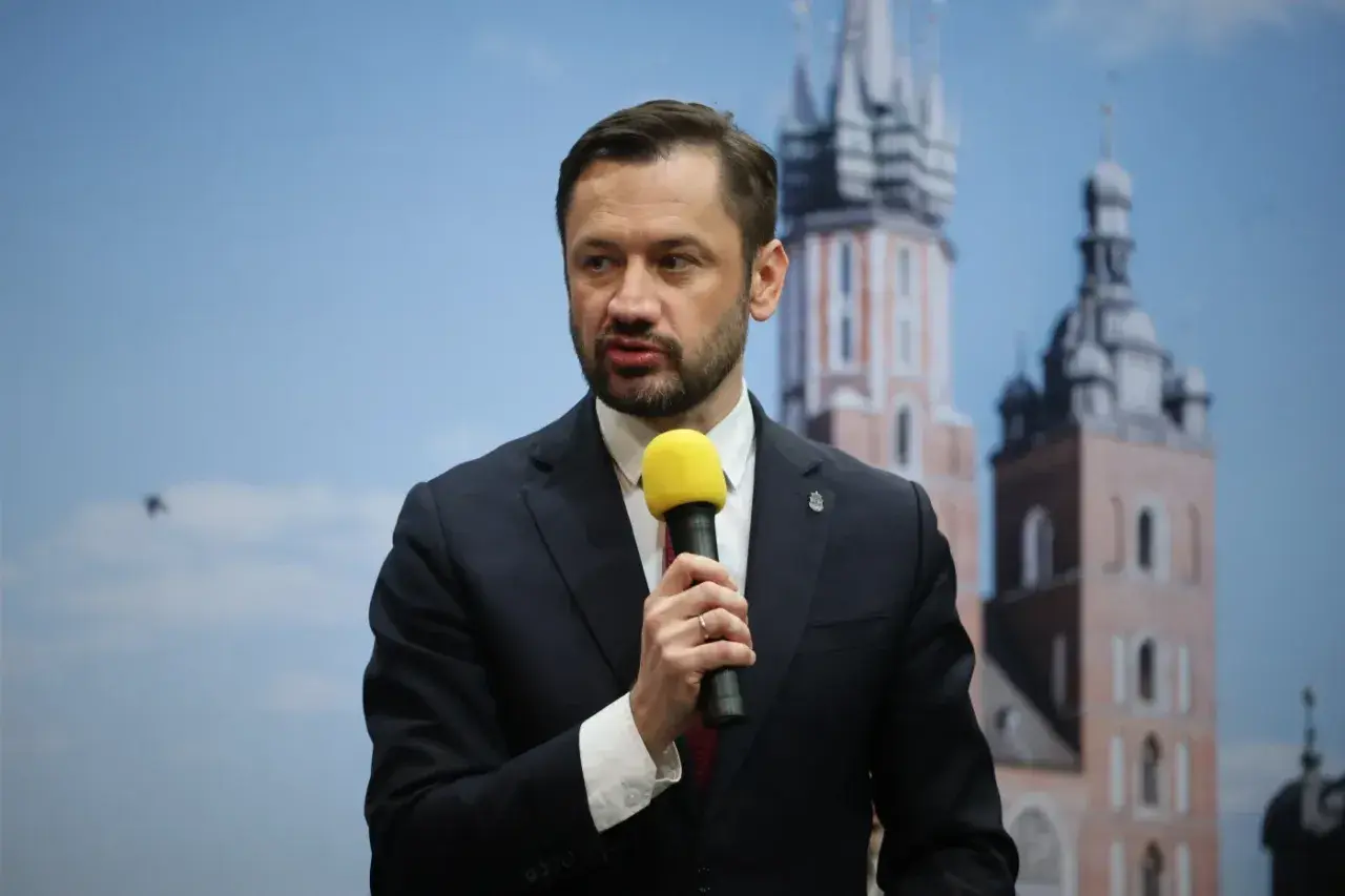 Tobiasz Bocheński, z mikrofonem w dłoni, przemawia na tle krakowskich wież. Jego rosnąca popularność sprawia, że jest uznawany za "czarnego konia" w wyścigu o urząd prezydenta.
