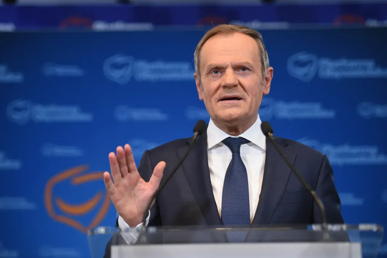 Donald Tusk w garniturze i krawacie przemawia przy mównicy z mikrofonami.