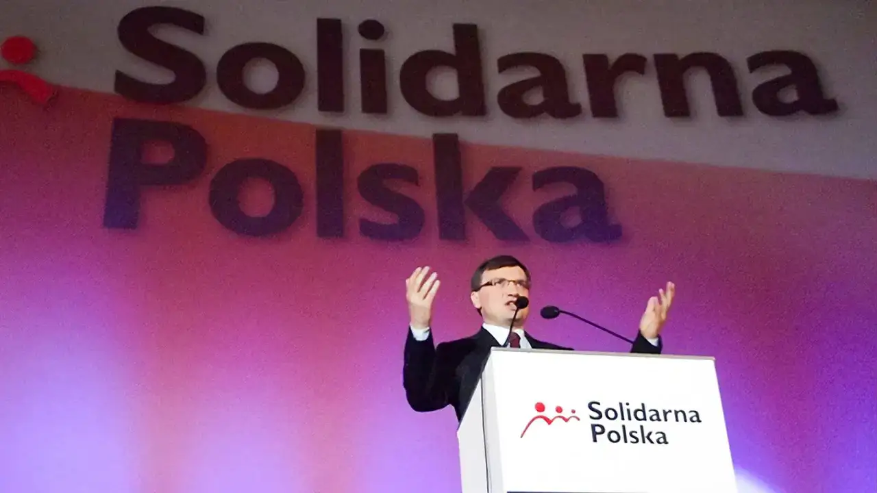 Mężczyzna przemawia na tle napisu 