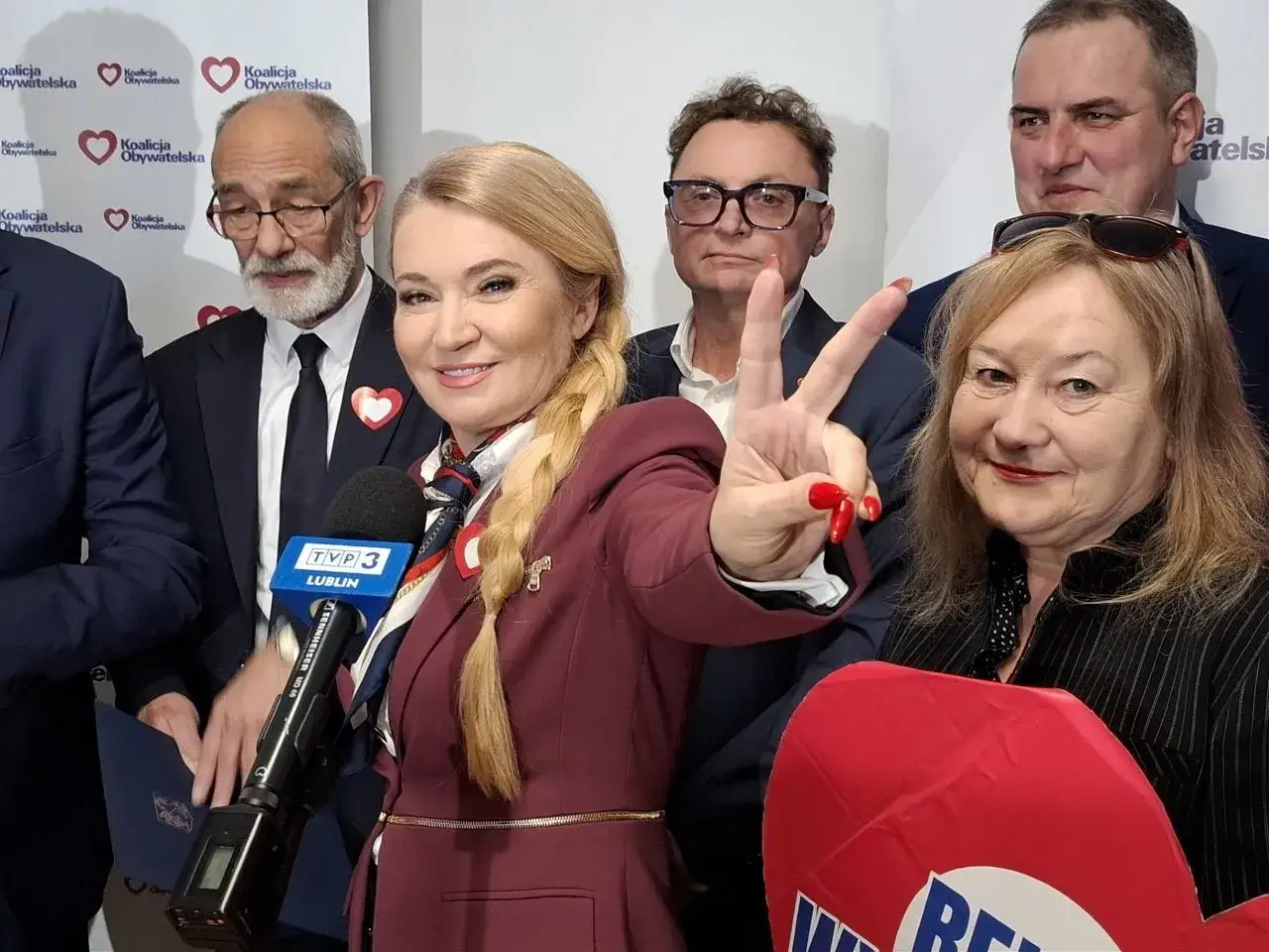 Kto z lubelskiej KO wygra bój o władzę 8 marca: Marta Wcisło czy Michał Krawczyk? Kobieta z mikrofonem TVP3 Lublin pokazuje znak zwycięstwa.