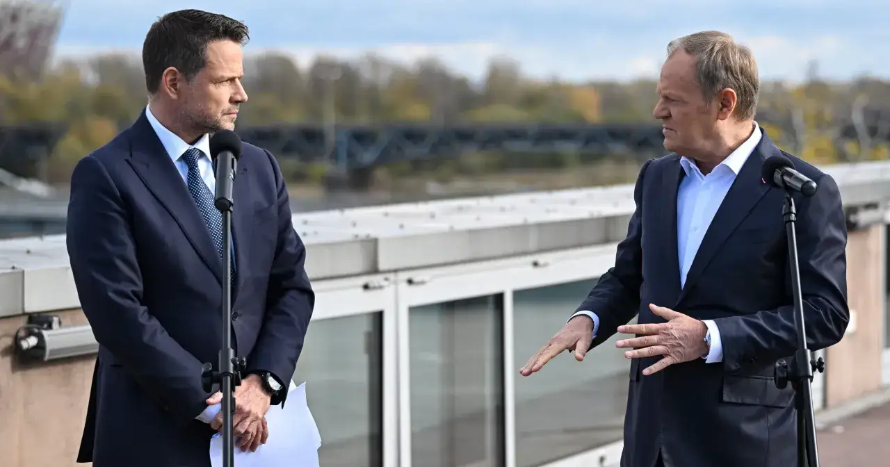 Czy Donald Tusk obawia się ambicji prezydenckich Rafała Trzaskowskiego? Politycy rozmawiają przy mikrofonach na tle mostu.