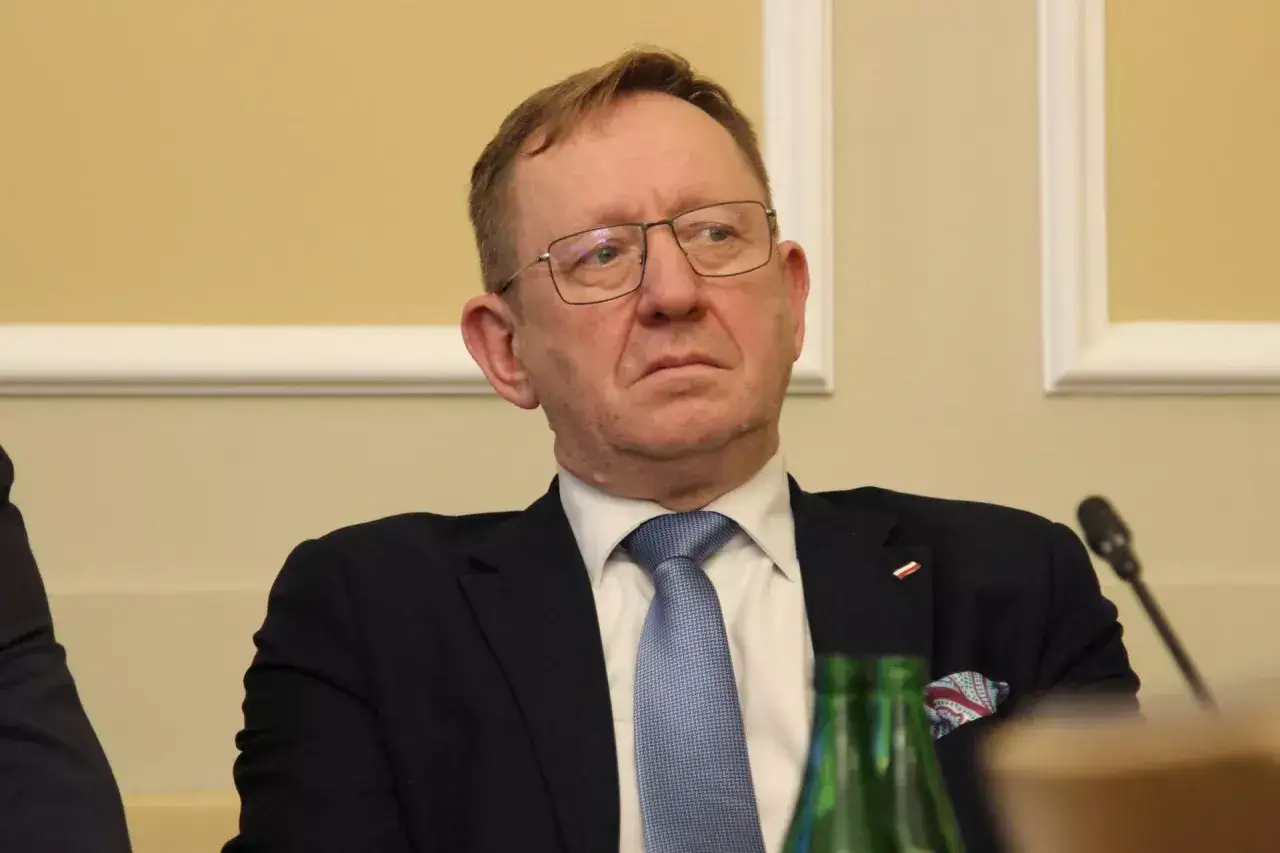 Mężczyzna w okularach, w garniturze i niebieskim krawacie, siedzi przy stole. Dyskutuje się, dlaczego Robert Telus i Rafał Romanowski zostali zawieszeni w prawach członka.