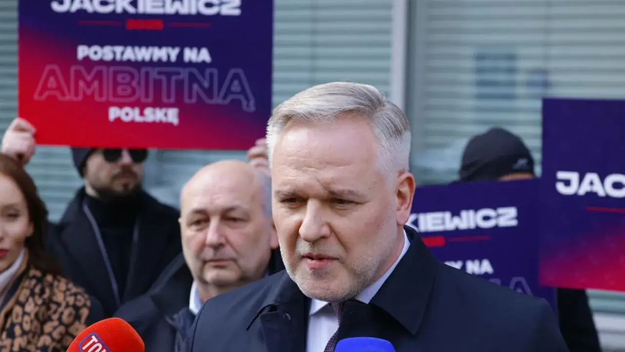 Polityk przemawia do mikrofonu. W tle transparent