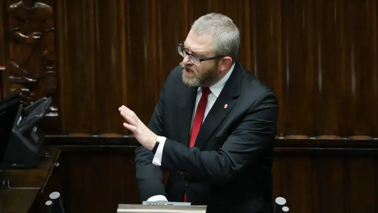 Grzegorz Braun w garniturze, z brodą i okularami, gestykuluje w sali sejmowej. Czy zostanie wykluczony z klubu za kontrowersyjne wypowiedzi o Izraelu?