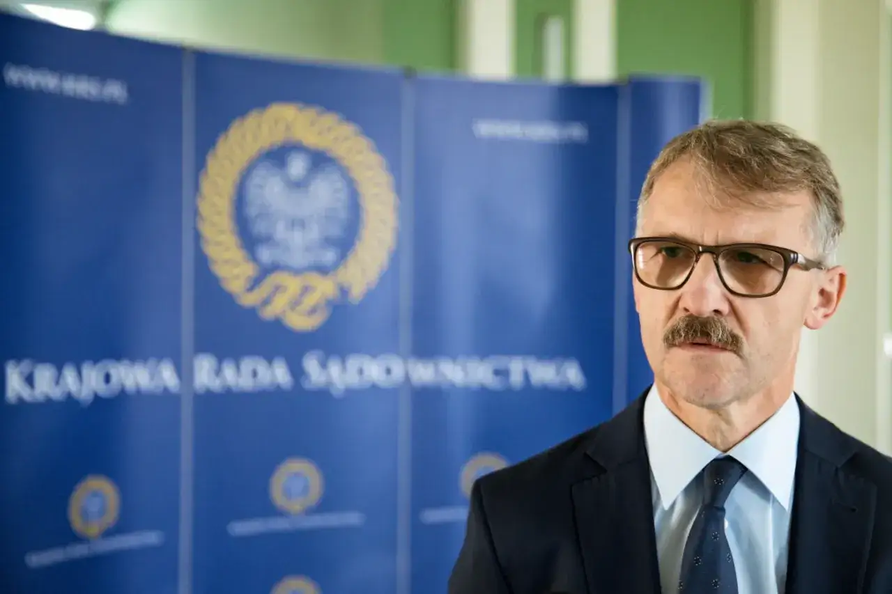 Mężczyzna w okularach i garniturze przed tablicą z napisem 