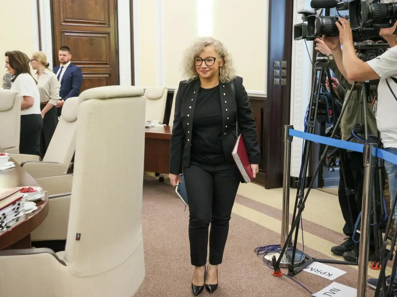 Kobieta z teczką idzie przez salę, gdzie kamery TV czekają na wyjaśnienie, dlaczego koalicja rządząca spiera się o ustawę dotyczącą związków partnerskich.