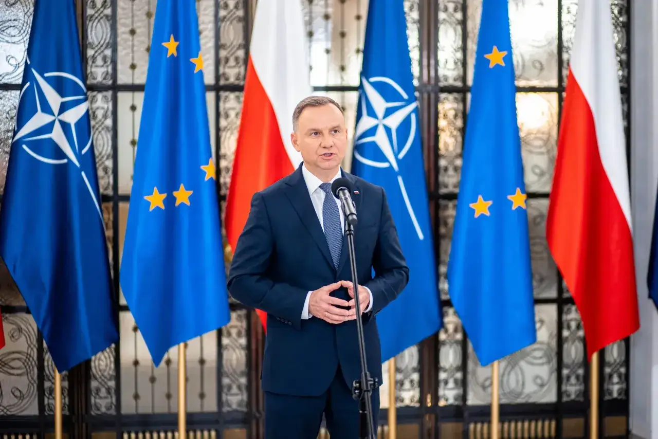 Prezydent Duda przemawia na tle flag Polski, NATO i UE. Choć nie znamy dokładnych danych, ile zarabia prezydent Duda, jego pensja jest ustalana ustawowo.