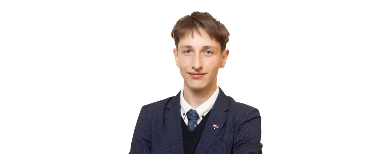 Młody działacz Ruchu Narodowego, który może zostać nową twarzą partii w sejmie, w granatowym garniturze i z przypinką z polską flagą.